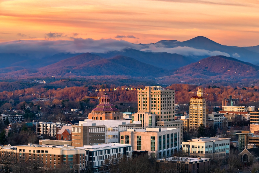 Asheville is nestled between Blue Ridge Mountains, the town with buildings only half as tall as the nature around with with clouds during sunset. 