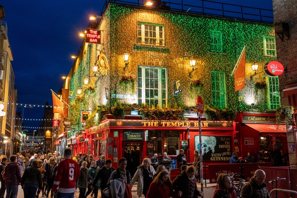 One of the cheapest places to fly from Tampa internationally is Dublin: in this photo the temple bar is lit up with Christmas lights and people crowd teh street enjoying a night out. 