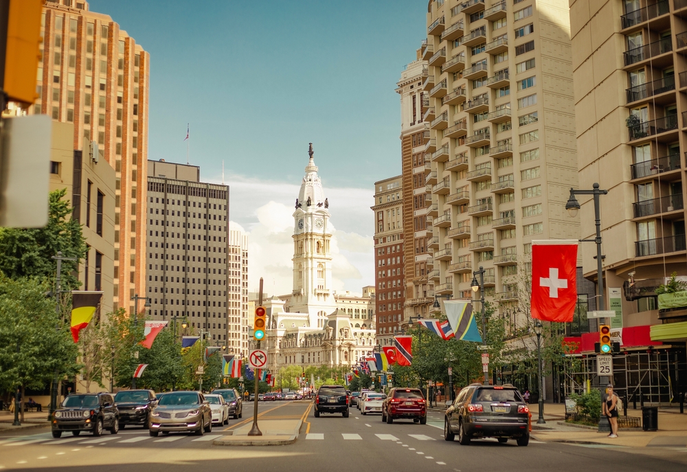 A shot of Philly shows the city's streets, lined with flags, historic and modern buildings together. 