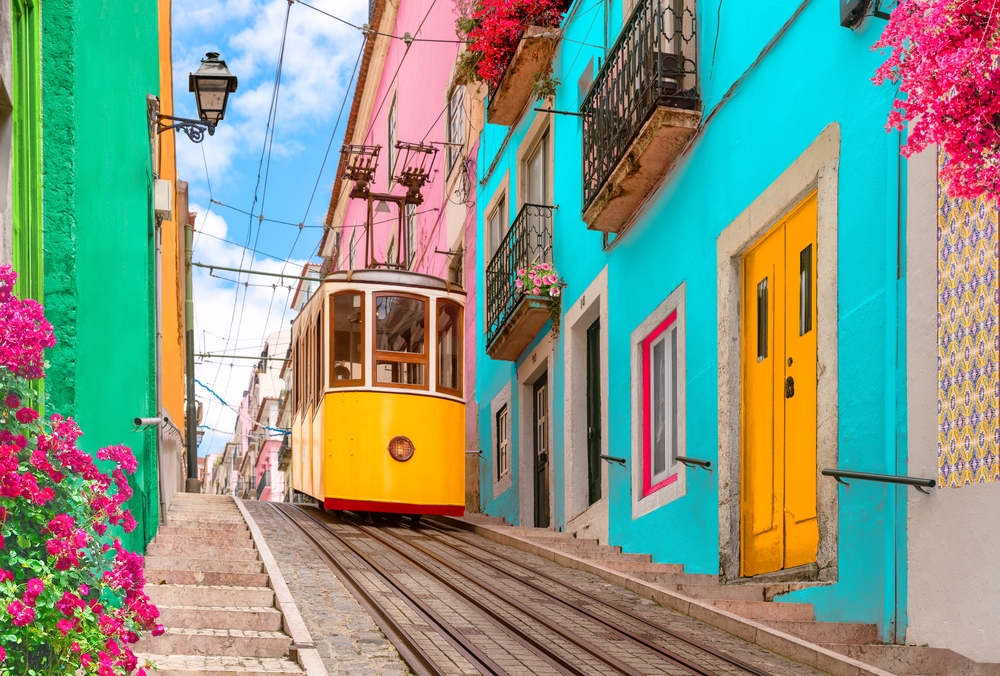 Yellow tram on a street with colorful houses and flowers on the balconies - Bica Elevator going down the hill of Chiado Lisbon 