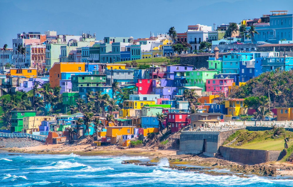 Colorful houses line the hillside over looking the beach in San Juan, Puerto Rico. The article is about cheapest places to fly from Florida.